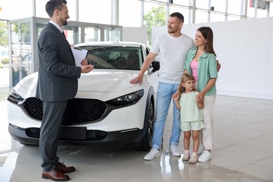 Photo of Salesman with clipboard showing new car to happy family in salon