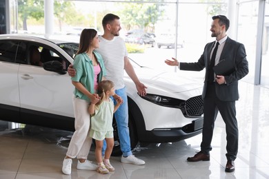 Photo of Salesman with clipboard showing new car to happy family in salon