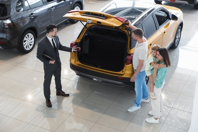 Photo of Salesman with clipboard showing new car to happy family in salon