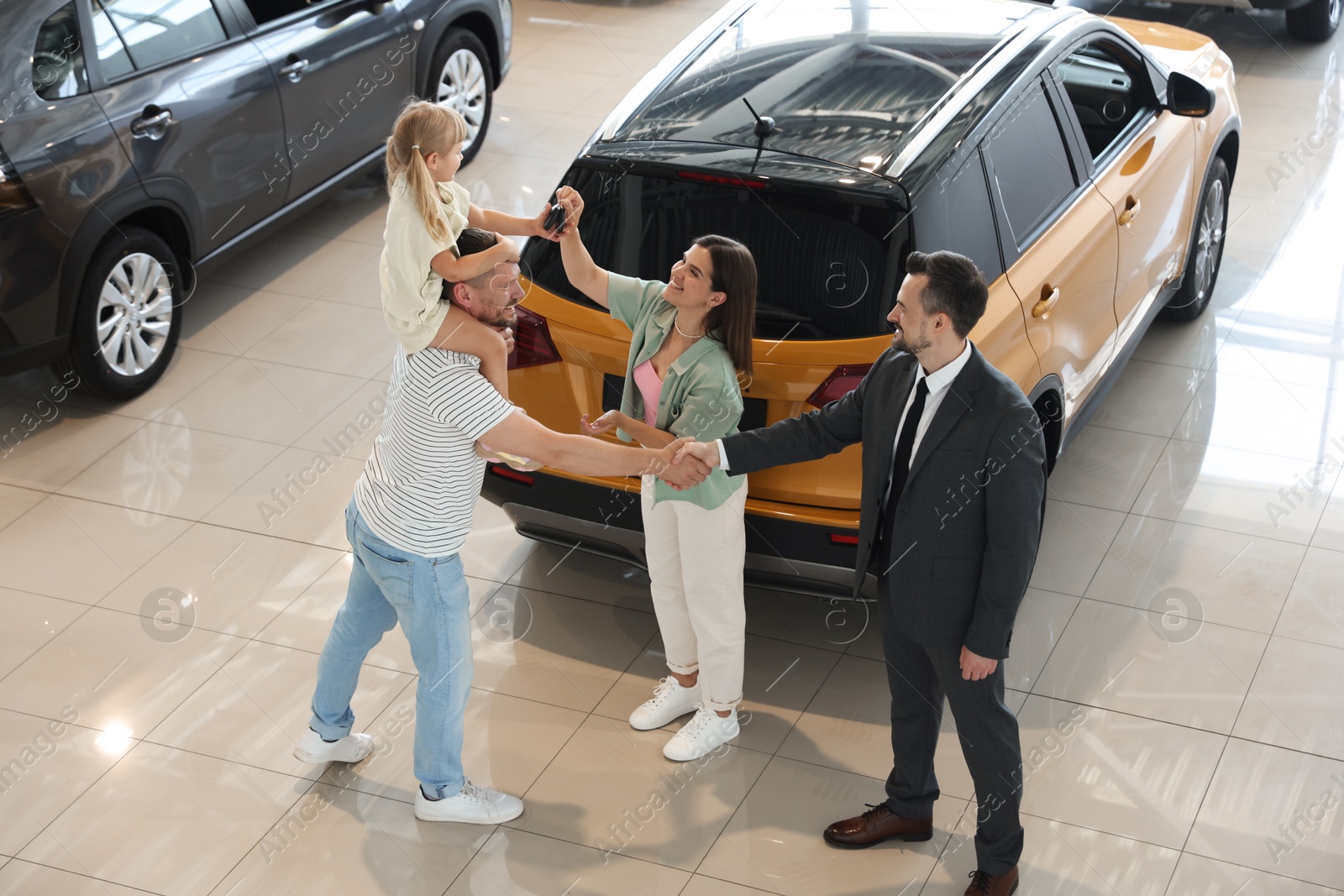 Salesman shaking hands with happy family near new car in salon Photo of Salesman shaking hands with happy family near new car in salon