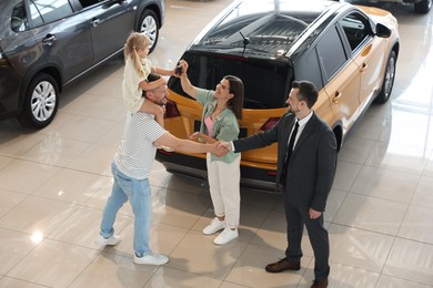 Photo of Salesman shaking hands with happy family near new car in salon