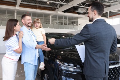 Photo of Salesman giving car key to happy family in salon