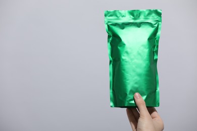 Photo of Woman holding blank zipper stand-up pouch on light grey background, closeup. Space for text