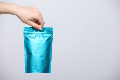 Photo of Woman holding blank zipper stand-up pouch on light grey background, closeup. Space for text