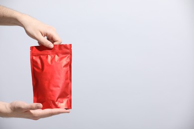 Photo of Woman holding blank zipper stand-up pouch on light grey background, closeup. Space for text