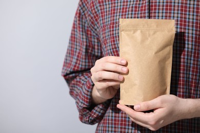 Photo of Woman holding blank zipper stand-up pouch on light grey background, closeup. Space for text