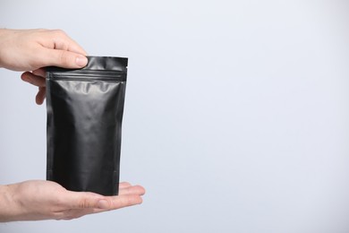 Photo of Woman holding blank zipper stand-up pouch on light grey background, closeup. Space for text