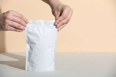 Photo of Woman holding blank zipper stand-up pouch at grey table against beige background, closeup. Space for text