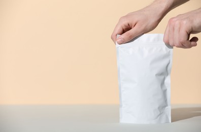 Photo of Woman holding blank zipper stand-up pouch at grey table against beige background, closeup. Space for text
