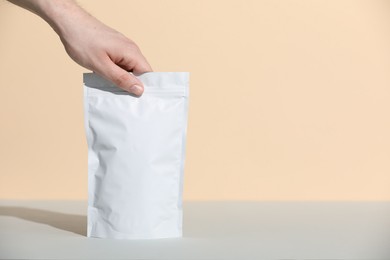 Photo of Woman holding blank zipper stand-up pouch at grey table against beige background, closeup. Space for text