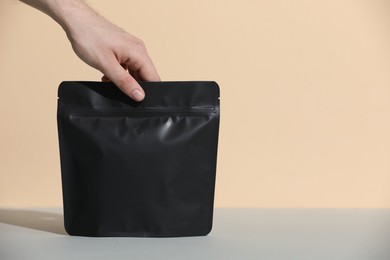 Photo of Woman holding blank zipper stand-up pouch at grey table against beige background, closeup. Space for text