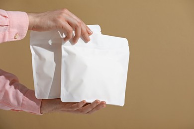 Photo of Woman holding blank zipper stand-up pouches on light brown background, closeup. Space for text