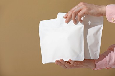 Photo of Woman holding blank zipper stand-up pouches on light brown background, closeup. Space for text