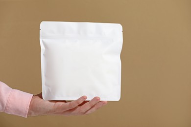 Photo of Woman holding blank zipper stand-up pouch on light brown background, closeup. Space for text