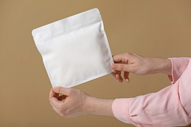 Photo of Woman holding blank zipper stand-up pouch on light brown background, closeup. Space for text