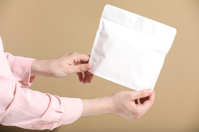 Photo of Woman holding blank zipper stand-up pouch on light brown background, closeup. Space for text