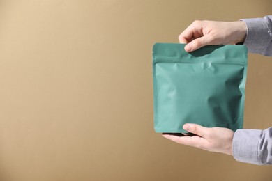 Photo of Woman holding blank zipper stand-up pouch on light brown background, closeup. Space for text