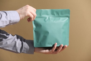 Photo of Woman holding blank zipper stand-up pouch on light brown background, closeup. Space for text