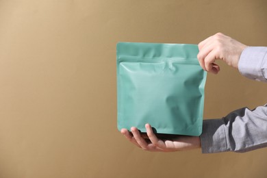 Photo of Woman holding blank zipper stand-up pouch on light brown background, closeup. Space for text