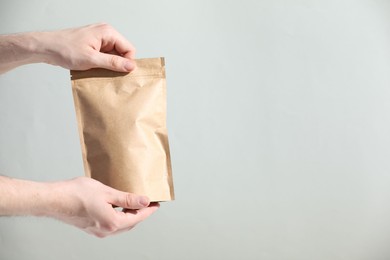 Photo of Woman holding blank zipper stand-up pouch on light grey background, closeup. Space for text