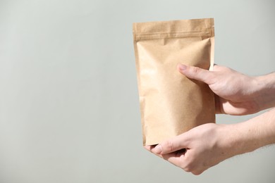 Photo of Woman holding blank zipper stand-up pouch on light grey background, closeup. Space for text