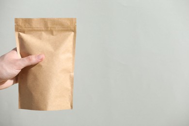 Photo of Woman holding blank zipper stand-up pouch on light grey background, closeup. Space for text