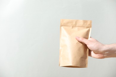 Photo of Woman holding blank zipper stand-up pouch on light grey background, closeup. Space for text