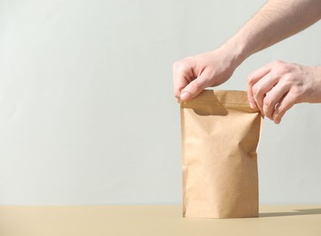 Photo of Woman holding blank zipper stand-up pouch on beige table against light grey background, closeup. Space for text