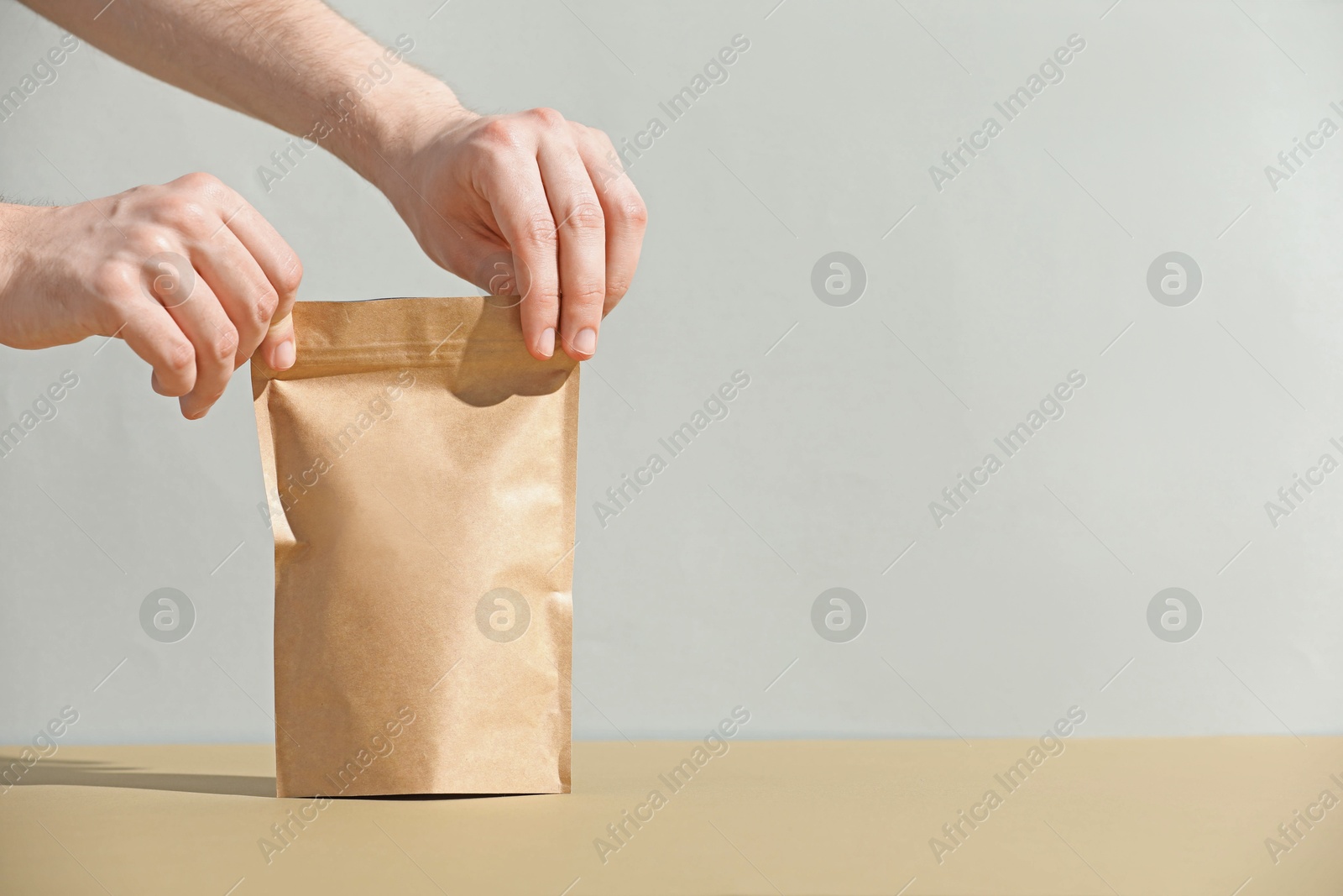Woman holding blank zipper stand-up pouch on beige table against light grey background, closeup. Space for text Photo of Woman holding blank zipper stand-up pouch on beige table against light grey background, closeup. Space for text