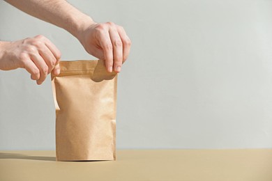 Photo of Woman holding blank zipper stand-up pouch on beige table against light grey background, closeup. Space for text