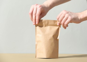 Photo of Woman holding blank zipper stand-up pouch on beige table against light grey background, closeup. Space for text
