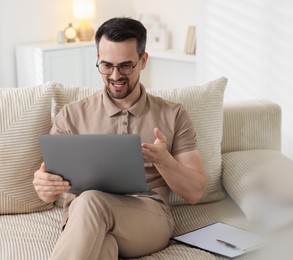 Photo of Professional psychologist having online consultation with his client via laptop on sofa indoors