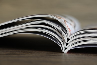 Photo of Different open magazines on wooden table, closeup