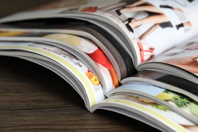 Photo of Different open magazines on wooden table, closeup