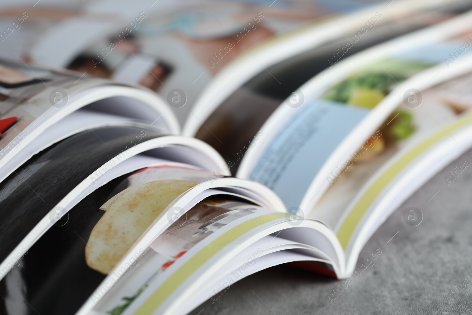 Different open magazines on grey table, closeup Photo of Different open magazines on grey table, closeup