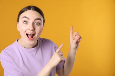 Photo of Surprised woman pointing at something on orange background, space for text