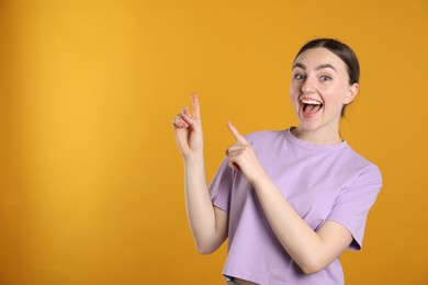 Photo of Surprised woman pointing at something on orange background, space for text