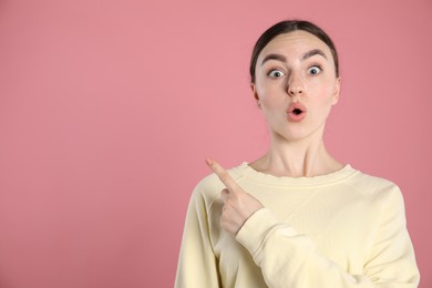 Photo of Surprised woman pointing at something on pink background, space for text