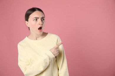 Photo of Surprised woman pointing at something on pink background, space for text