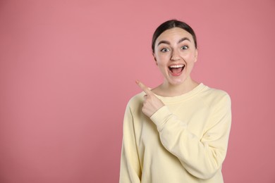 Photo of Surprised woman pointing at something on pink background, space for text