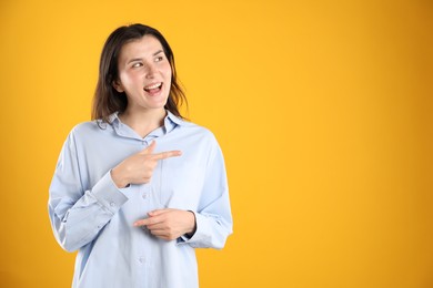Photo of Surprised woman pointing at something on orange background, space for text
