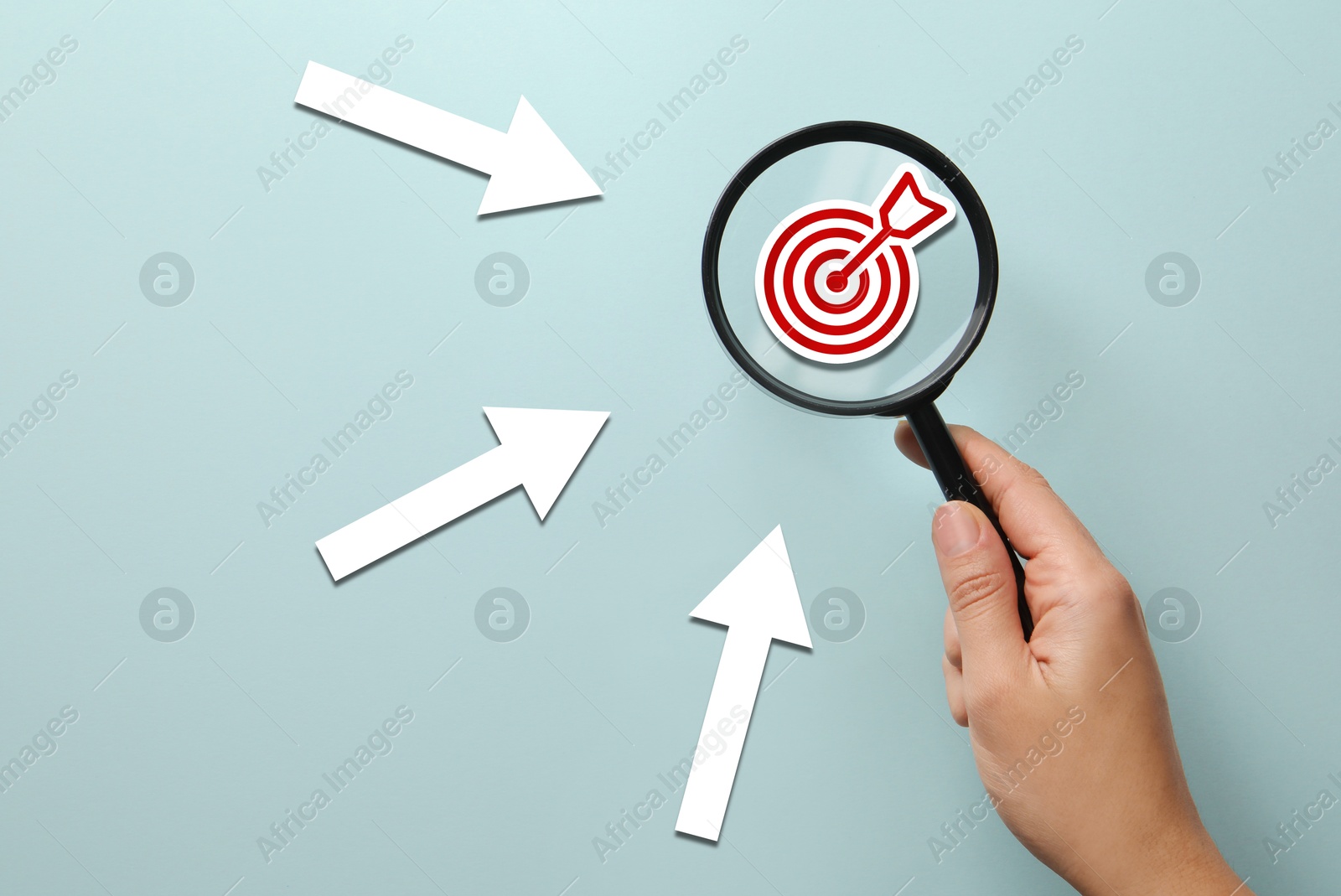 Woman holding magnifying glass with target inside against light blue background, closeup. Arrows pointing at magnifier Image of Woman holding magnifying glass with target inside against light blue background, closeup. Arrows pointing at magnifier