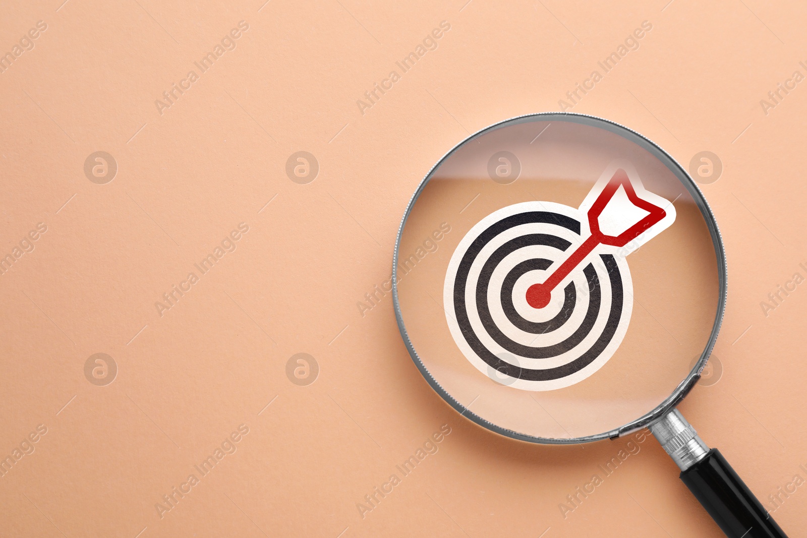 Magnifying glass over target with arrow on pink beige background, top view Image of Magnifying glass over target with arrow on pink beige background, top view