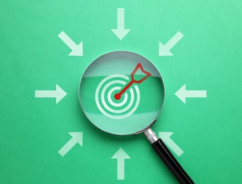 Image of Magnifying glass over target on green background, top view. Arrows pointing at magnifier