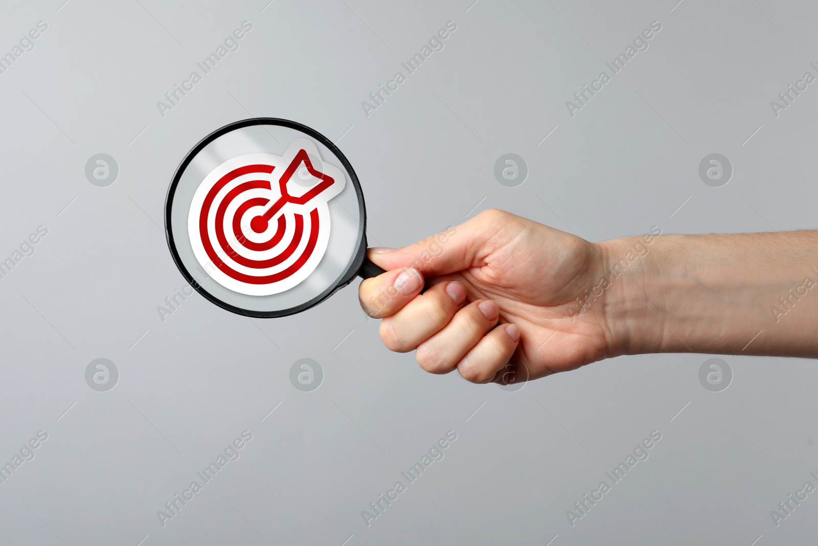 Image of Woman holding magnifying glass with target and arrow inside against grey background, closeup