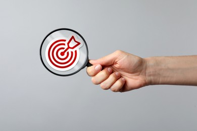 Image of Woman holding magnifying glass with target and arrow inside against grey background, closeup