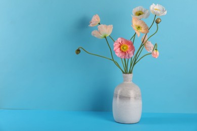 Photo of Beautiful poppy flowers in vase on light blue background, closeup. Space for text