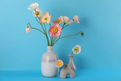 Photo of Beautiful poppy flowers in vases on light blue background, closeup