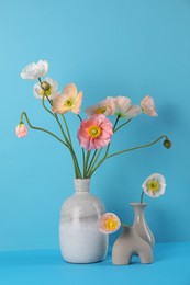 Photo of Beautiful poppy flowers in vases on light blue background, closeup