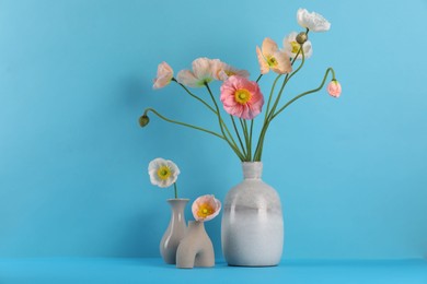 Photo of Beautiful poppy flowers in vases on light blue background, closeup